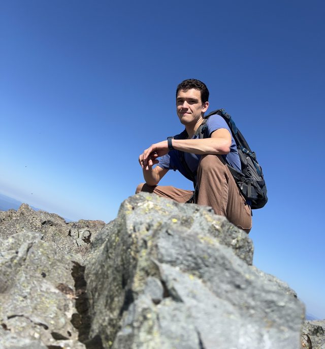Justin crouching on a rock in front of a blue sky